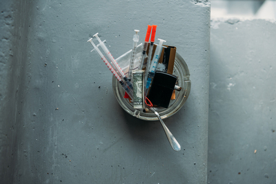Syringes and rolled dollar bills in a glass ashtray.