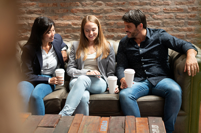 Three people sitting on a couch drinking coffee.