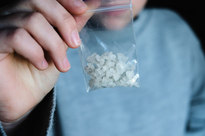 Person holding a small clear bag with drugs.