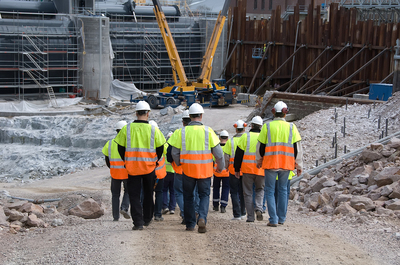Group of workers with reflective vests and hard hat entering a construction site.