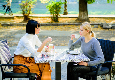 Two women sitting at a cafe outside drinking coffee.