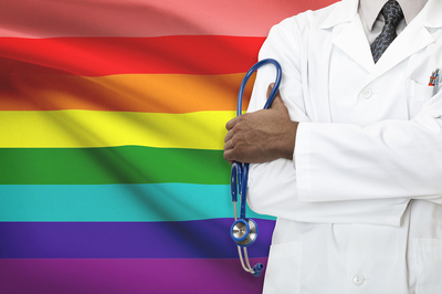 Medical doctor standing in front of a rainbow flag.