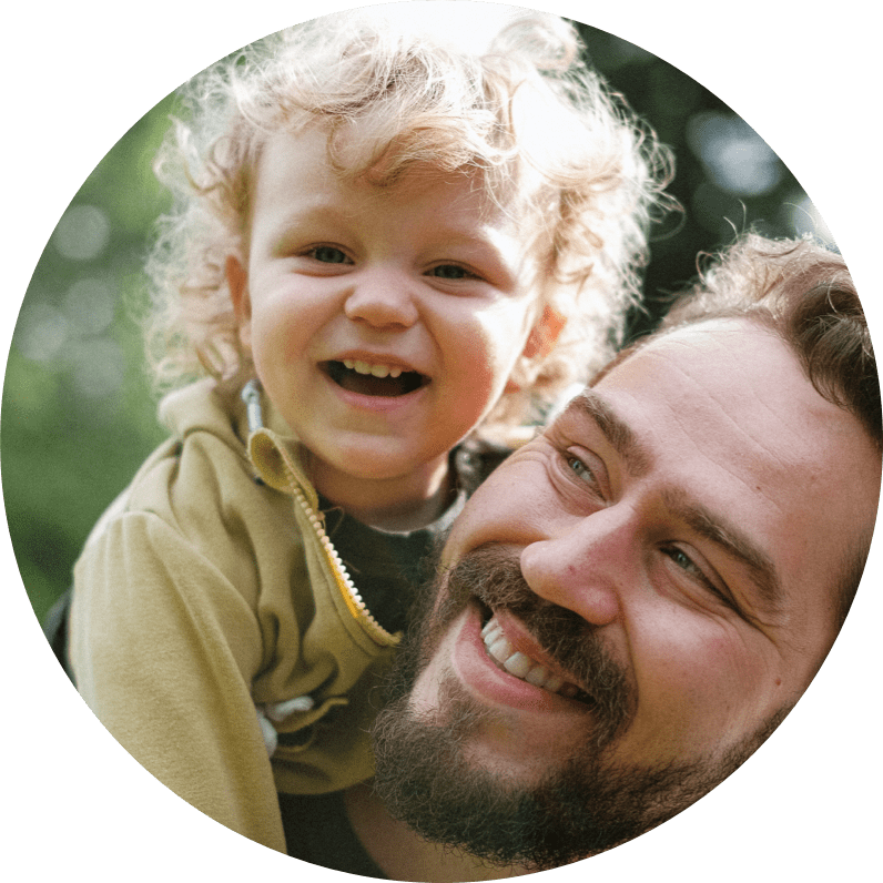 Smiling man with a beard holds a smiling small child with curly blonde hair